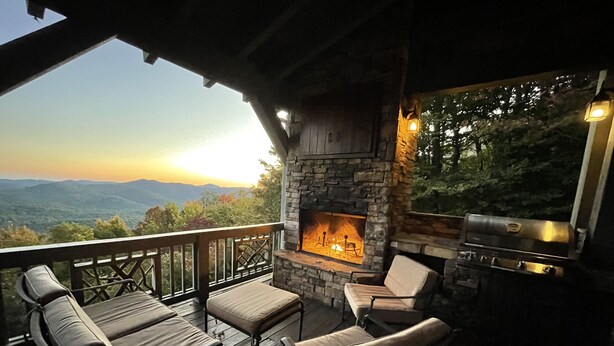 A deck with outdoor seating, a stone fireplace, and a grill.