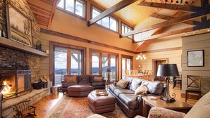 A cozy living room with a fireplace, leather sofas, and a large window overlooking a scenic view.