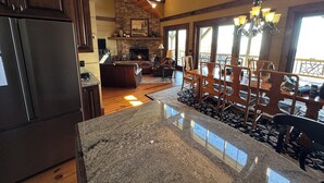 A spacious kitchen with granite countertops, a stone fireplace, and a dining area with wooden chairs and a chandelier.