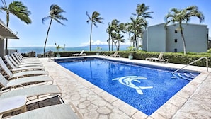 A swimming pool with lounge chairs and palm trees, overlooking a body of water. - Oceanfront, AC!, king bed, kayaks, pickleball, and beach stuff all included! (Kaunakakai)