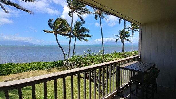 A balcony with a view of the ocean and palm trees. - Oceanfront, AC!, king bed, kayaks, pickleball, and beach stuff all included! (Kaunakakai)
