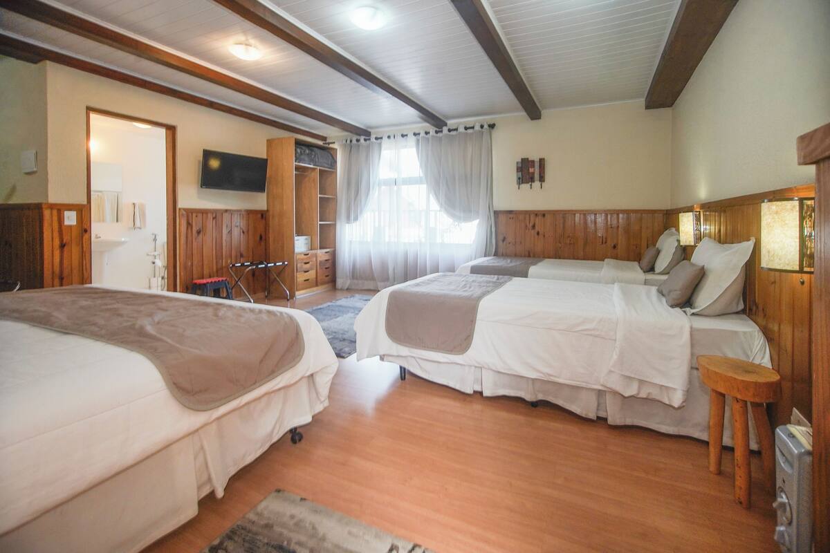 Une chambre avec trois lits, un plancher en bois, un téléviseur fixé au mur et une fenêtre avec des rideaux.
