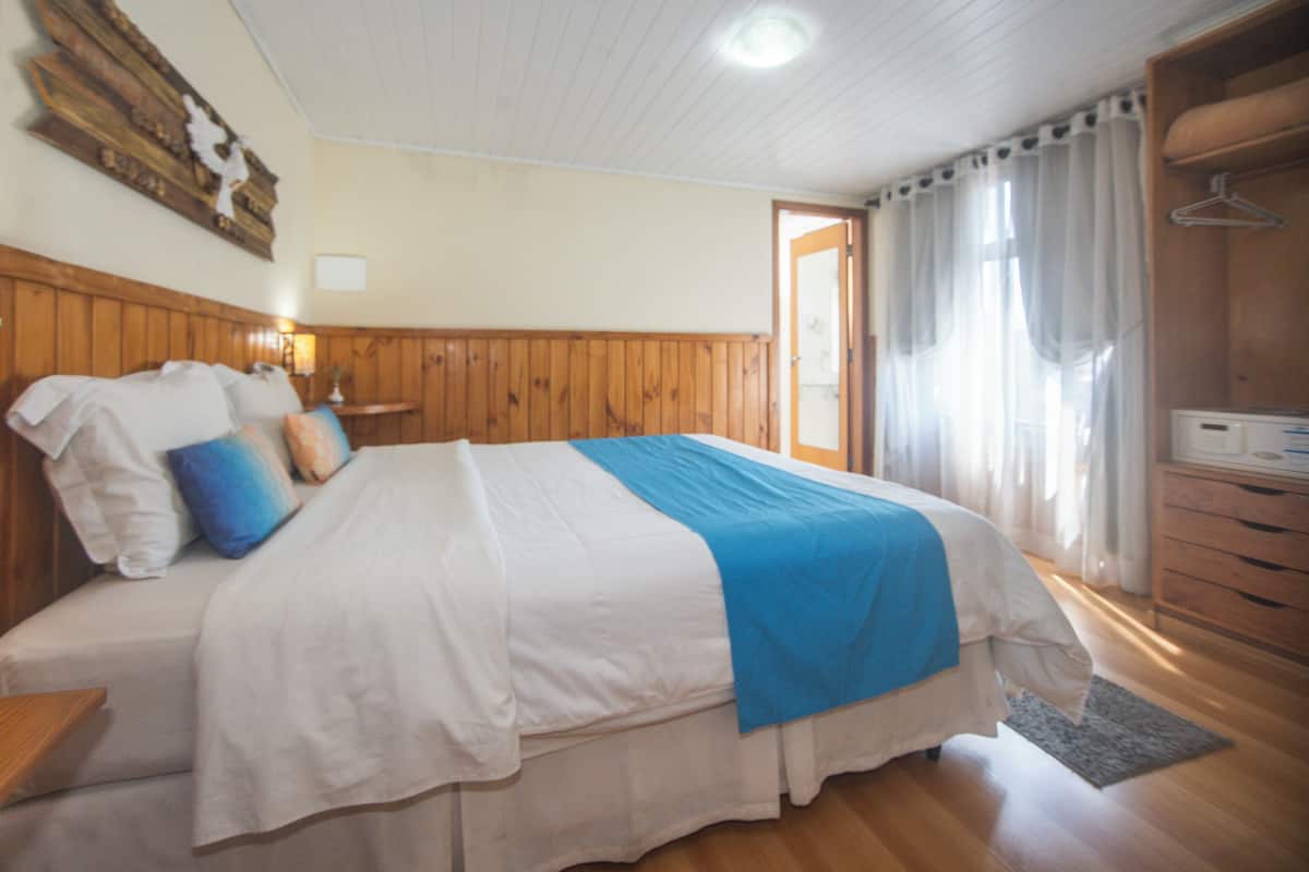 Une chambre à coucher avec une tête de lit en bois, un lit avec une literie blanche et un élément décoratif bleu, une table de chevet avec une lampe, et une armoire en bois.