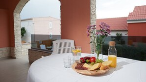 A table set for breakfast with a variety of foods and drinks, a vase of flowers, and a view of buildings through an archway. - Villa Adria II, apartment B3, with 2 swimming pools (Pag)