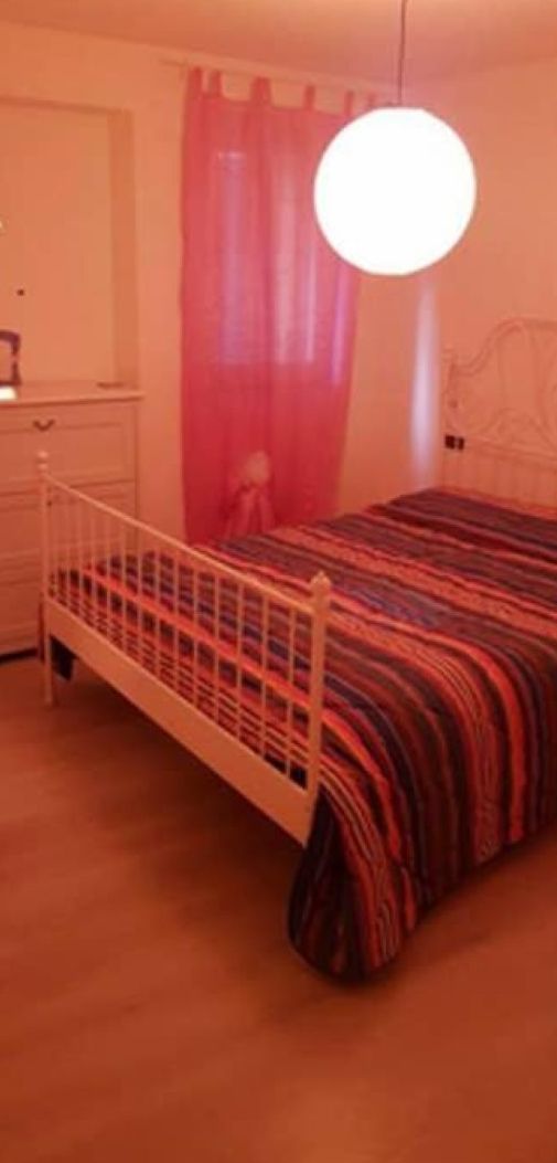 A bedroom with a single bed, a nightstand, a dresser, and a hanging light fixture.