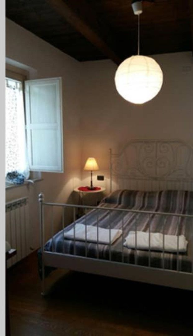 Una camera da letto con un letto, un comodino con una lampada, una finestra e un termosifone.