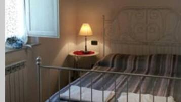Una camera da letto con un letto, un comodino con una lampada, una finestra e un termosifone.
