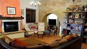 Una sala de estar acogedora con chimenea, asientos cómodos, televisión y una estantería llena de libros y objetos decorativos.