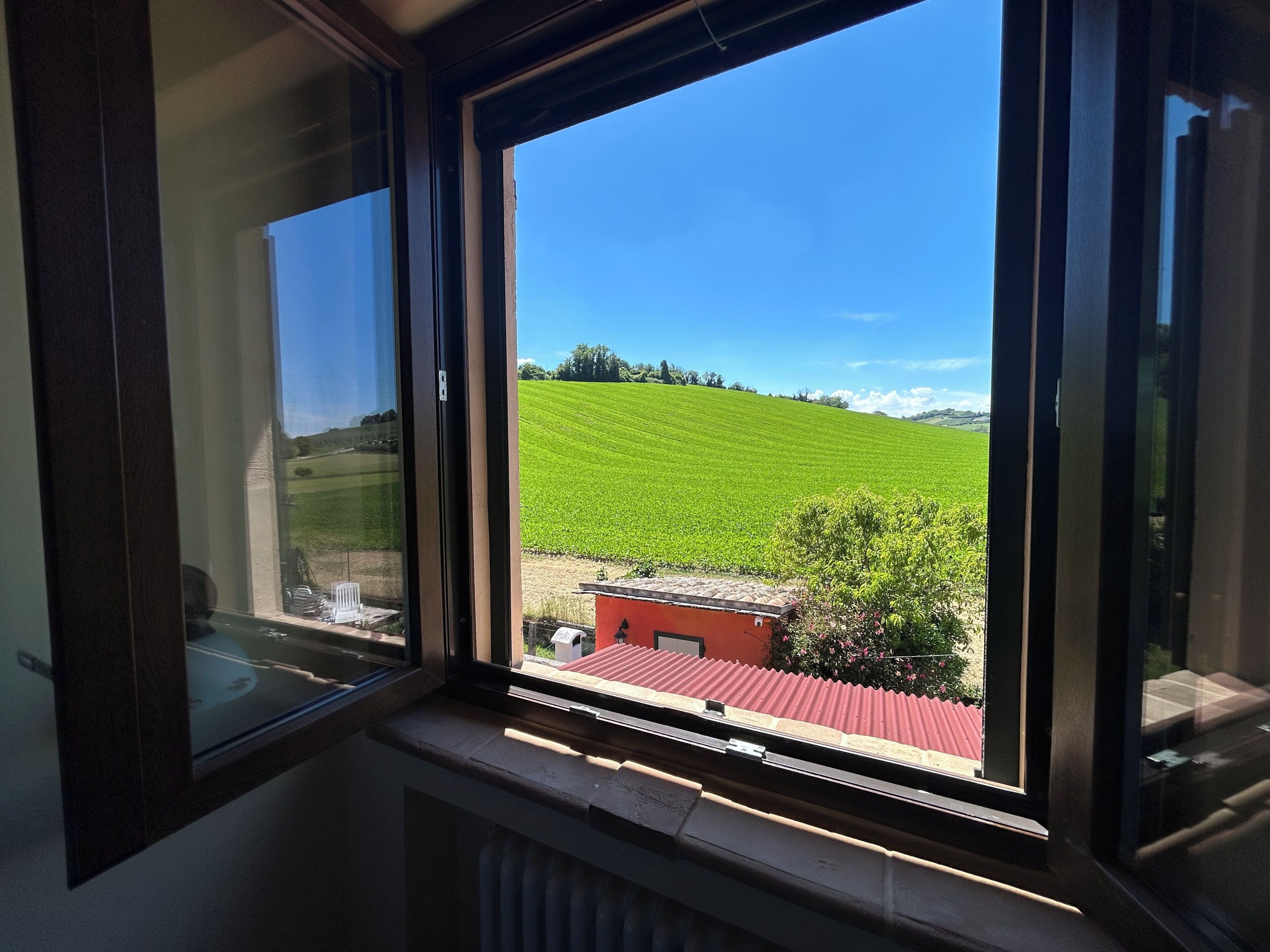 Ein Fenster mit Blick auf ein grünes Feld und ein Gebäude mit rotem Dach.
