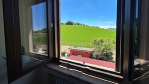 Una ventana con vistas a un campo verde y un edificio de techo rojo.