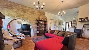 Una sala de estar con chimenea de ladrillo, un sofá, un televisor y una araña.