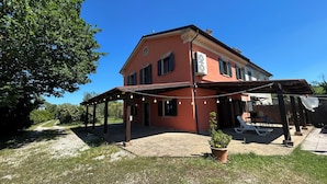 Una casa de dos pisos con un porche cubierto, mobiliario exterior y un jardín.