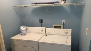 Un espace buanderie comprenant deux machines à laver blanches, un  étendoir et une bouteille de lessive.