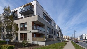 Ein modernes Mehrfamilienhaus mit Balkonen, einem gepflasterten Bürgersteig und blauem Himmel.
