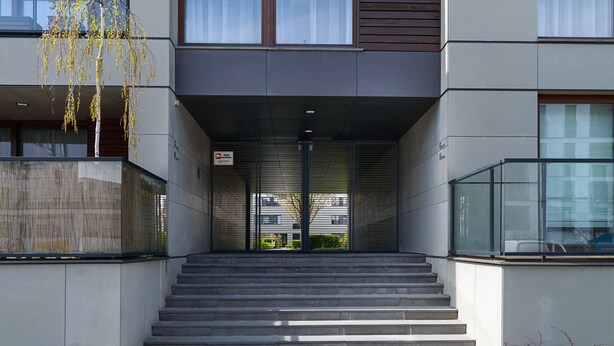 Ein moderner Gebäudeeingang mit einer Treppe aus Beton, die zu einer Glastür führt.