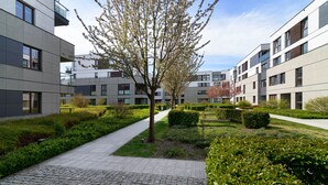 Ein moderner Gebäudekomplex mit mehreren Stockwerken, einem zentralen Innenhof mit einem Baum und einem gepflasterten Weg.