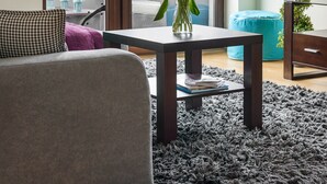 Ein Wohnzimmer mit Sofa, Couchtisch mit einer Tulpenvase, einem blauen Sitzsack und Blick durch eine Glastür auf einen Balkon.