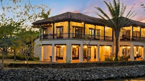 A two-story building with balconies, a stone wall in front, and a body of water in the foreground.