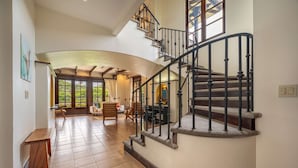 A spacious living area with a curved staircase and large windows.