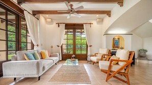 A spacious living room with a sofa, chairs, a coffee table, and large windows with curtains.