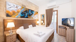 Una camera d'albergo con un letto grande, una scrivania con televisore, un quadro appeso al muro e una finestra con tende.