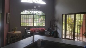 A room with a dining area, a small table with a plant, and a window with a view of greenery.