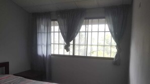 A bedroom with a single bed, a window with curtains, and a radiator.