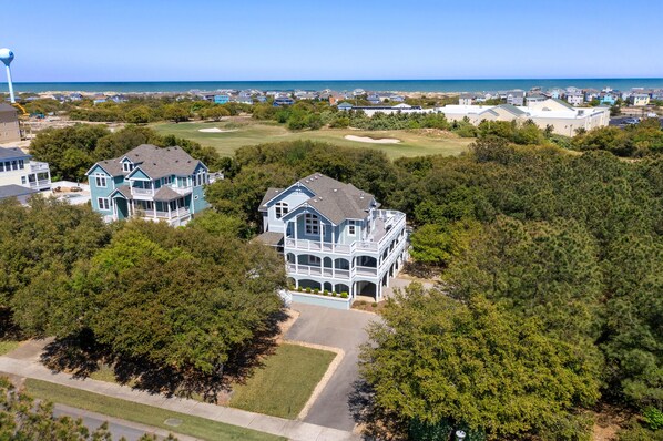 A large, two-story house with a balcony, surrounded by dense trees and a golf course. - Seadog: Private Pool, Hot Tub, Rec Room (Corolla)