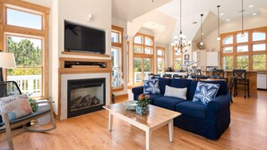 A spacious living room with a fireplace, a large TV, and a blue sofa. - Seadog:  Private Pool, Hot Tub, Rec Room (Corolla)