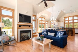 A spacious living room with a fireplace, a large TV, and a blue sofa. - Seadog: Private Pool, Hot Tub, Rec Room (Corolla)