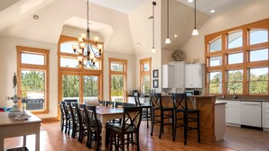 A spacious kitchen with wooden flooring, large windows, and a central island with bar stools. - Seadog:  Private Pool, Hot Tub, Rec Room (Corolla)