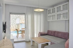 Una sala de estar moderna con una pared de piedra, un sofá, una mesa de centro y vista a una piscina a través de una puerta de vidrio.