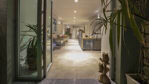 Un interior moderno con una puerta de cristal que da a un pasillo, una recepción y un comedor con sillas y mesas.
