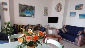 En stue med sofa, spisebord med blomster, fjernsyn og billeder på væggen.