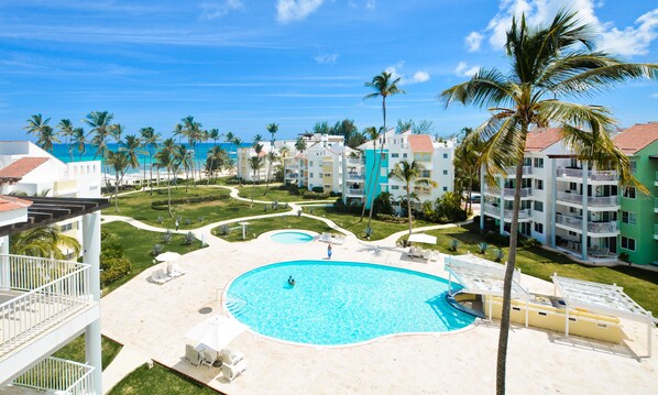 Un resort con piscina central, varias edificaciones y palmeras.