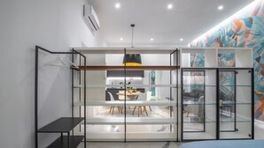 A modern bedroom with a bed, a desk, and a dining area visible through a glass partition. - Frida Loft (Syracuse)