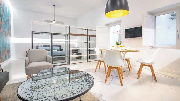 A modern living room with a glass coffee table, white chairs, a black pendant light, and a large window. - Frida Loft (Syracuse)