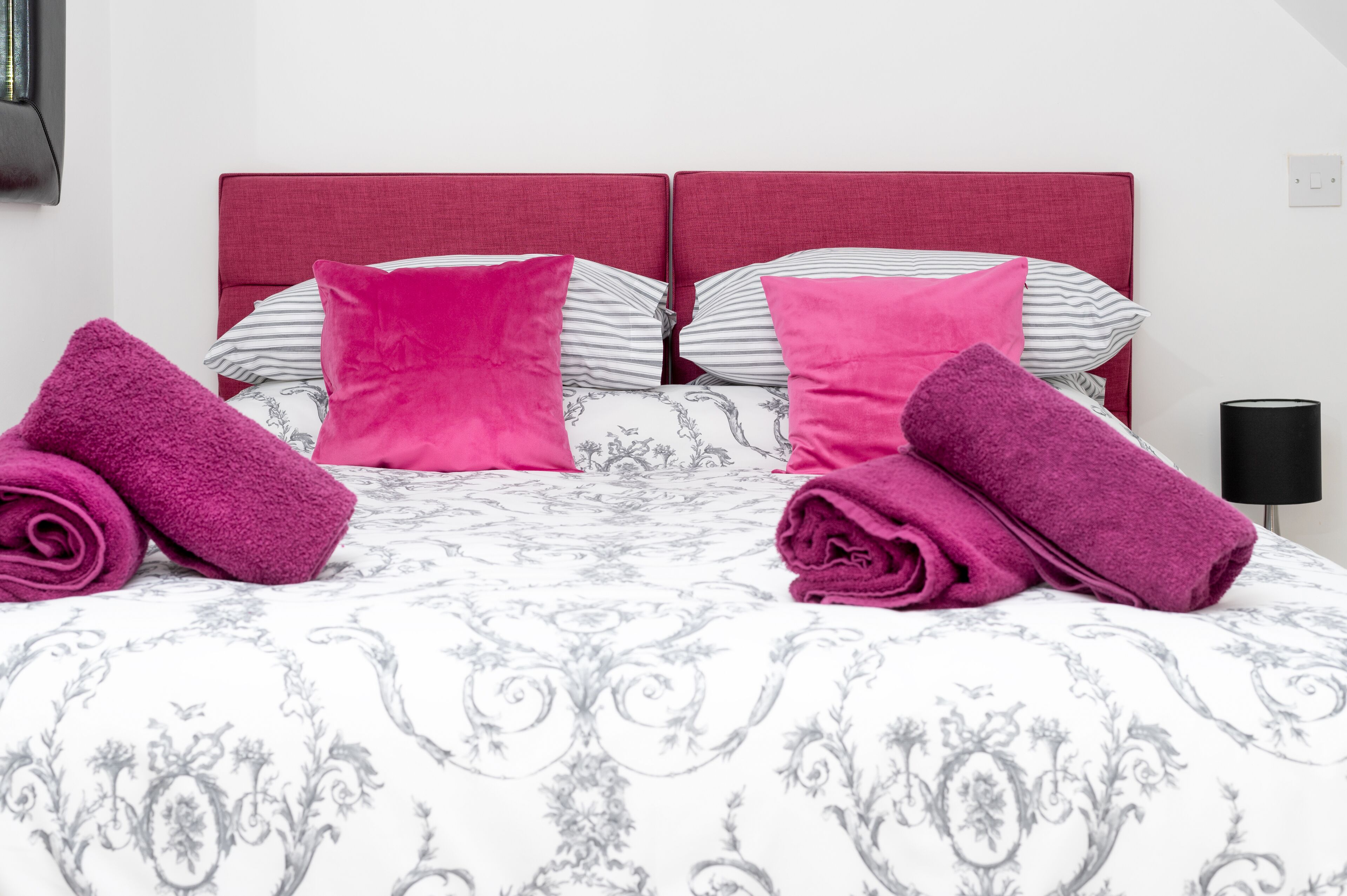 A neatly made bed with a patterned bedspread, two pillows, and two rolled towels.