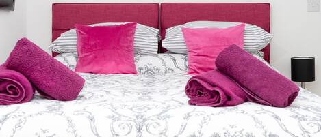 A neatly made bed with a patterned bedspread, two pillows, and two rolled towels.