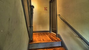 Un escalier étroit avec un plancher en bois, une rampe métallique et une porte portant le numéro 1E.
