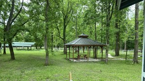 Un gazebo in un parco con tavolo da picnic, circondato da alberi e recinzione.