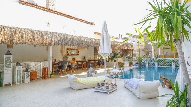 Un área junto a la piscina con techo de paja, sillones de descanso y zona de comedor.