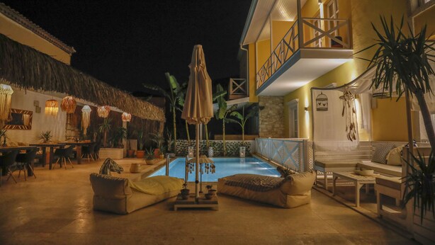 An outdoor pool area with lounge chairs and umbrellas, surrounded by potted plants and a thatched-roof structure. - Adacan Alacatı (Cesme)