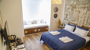 Un dormitorio ordenado con cama, cómoda de madera, ventana con vistas y pared de piedra decorada con macramé.