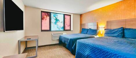 A hotel room with two beds, a flat-screen TV, a small table, and a window with abstract art.