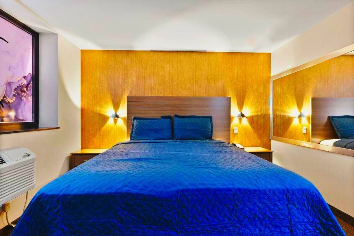 Ein Hotelzimmer mit einem großen Bett, einem hölzernen Kopfteil, zwei Nachttischlampen und einer Wand-Klimaanlage.