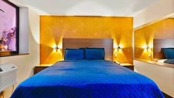 Habitación de hotel con una cama grande, cabecero de madera, dos lámparas de noche y un aire acondicionado instalado en la pared.