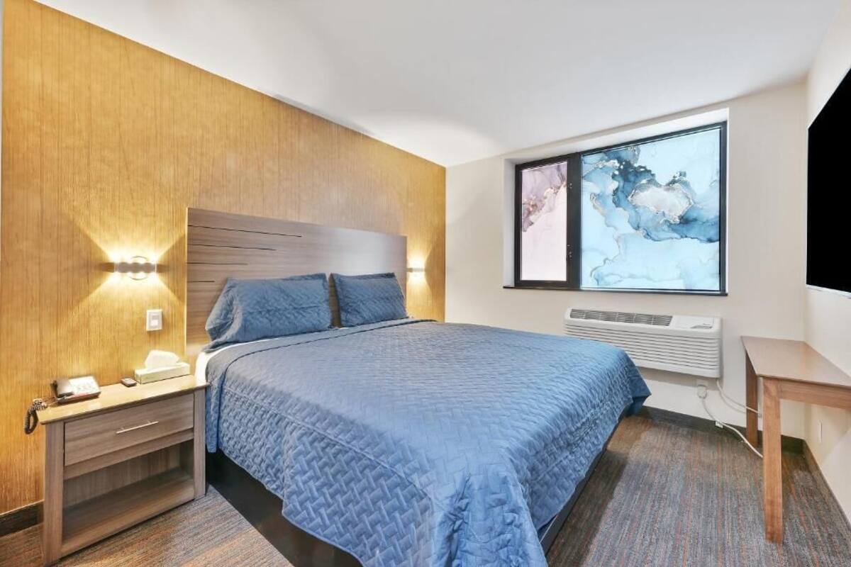 Ein Hotelzimmer mit Bett, Nachttisch, Lampe und einem Kunstwerk an der Wand.