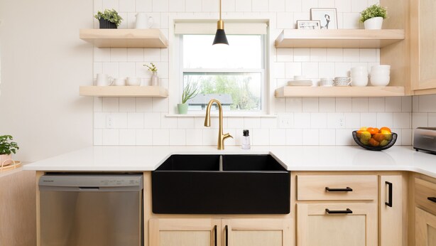 A modern kitchen with white tiled walls, wooden cabinets, and a black sink. There are two wooden shelves above the sink, each holding various kitchen items. A window with a white blind is centered above the sink, and a black pendant light hangs above it.