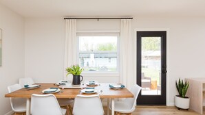 A dining area with a wooden table, white chairs, and a window with curtains.